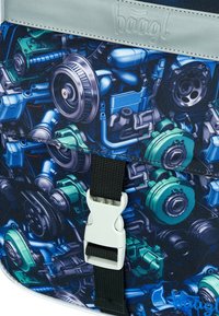 Zaino con un motivo di parti di motore blu e verde, dotato di un cappuccio superiore grigio e una chiusura a fibbia bianca su un tessuto texturizzato.