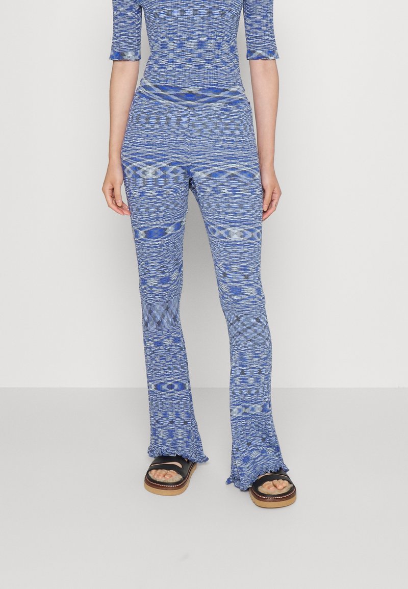 Ensemble tricoté bleu en deux pièces comprenant un haut ajusté et un pantalon évasé avec des rayures horizontales et des motifs texturés. Les détails incluent des ourlets à volants.