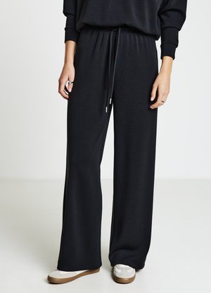 Schwarze Hosen mit weitem Bein aus weichem Stoff, mit elastischem Bund und Kordelzug, in entspannter Passform. Gestylt mit hellfarbenen Sneakern.