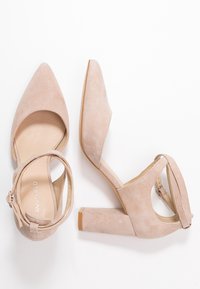 Beiga mockaskor med hög klack, spetstå och ankelsnodd, samt blockklack. Slät textur med en utskärning på sidorna.