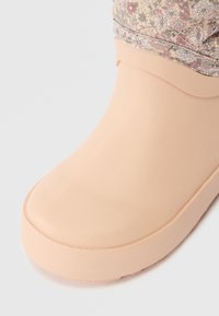 Bota de borracha rosa clara com uma superfície lisa e um bico arredondado. Cuff em tecido com padrão floral na parte superior, proporcionando um contraste texturizado.