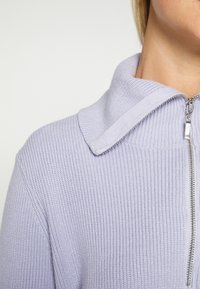 Maglione zip-up viola chiaro con una texture a coste e un ampio colletto. Presenta una cerniera argentata e un tessuto morbido a maglia.