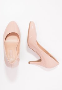Ljusrosa patenterade läderhögklackade skor med spetsig tå och smal klack. Slät textur och minimalistisk design med en avsmalnande siluett.