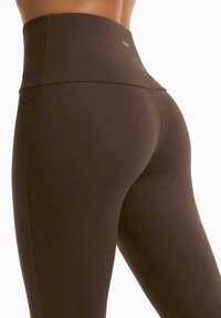 Korkeavyötäröiset, tummanruskeat legginsit joustavasta materiaalista, joissa on sileä pinta ja minimalistinen muotoilu ilman näkyviä saumoja.