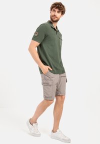 Groene poloshirt met een kraag en borstzak, gecombineerd met lichtgrijze cargoshorts met zijzakken, gedragen met witte sneakers.