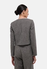Veste courte à carreaux noir et blanc avec des manches longues, présentant un dos droit et un tissu texturé, associée à un pantalon assorti.