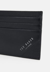 Black leather cardholder with multiple slots, featuring a textured accent and embossed logo in silver at the bottom corner.