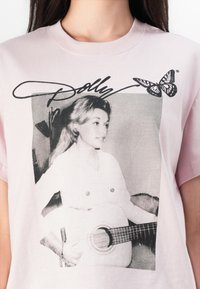 Rosa bomull t-skjorte med et svart-hvitt bilde av en kvinne med en gitar, utsmykket med teksten "Dolly" og et sommerfuglmotiv.