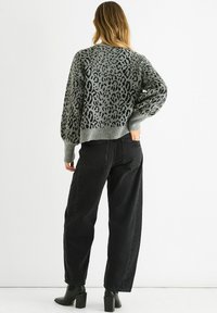 Gray knit sweater with black animal print, featuring a relaxed fit and ribbed cuffs, paired with high-waisted black jeans and black ankle boots.