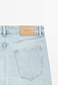 Light blue denim jeans featuring a rectangular tan leather patch with "Massimo Dutti" embossed. Includes a back pocket with stitching details.