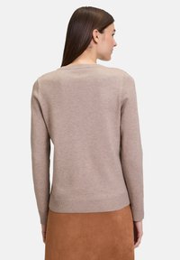 Maglione beige con maniche lunghe, scollatura rotonda e polsini e orlo rigati; realizzato in materiale morbido, indossato con una gonna in suede marrone.