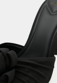 Scarpa nera con tacco alto, caratterizzata da un tessuto liscio e strutturato con un dettaglio annodato sulla fascia della punta e un tacco lucido.