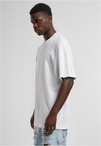 Liela baltā kokvilnas T-kreklu ar punktētu logo rakstu krūšu rajonā. Valkāts ar izbalējušām gaiši ziliem džinsiem šortiem.