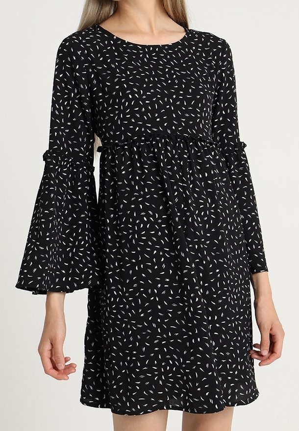 Vestido negro con mangas acampanadas, que presenta una cintura fruncida y un patrón abstracto blanco a lo largo de la tela. Textura suave.