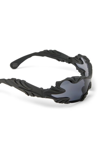 Zwarte zonnebril met donker getinte glazen, voorzien van gebeeldhouwde, vlamachtige decoratieve monturen en pootjes.