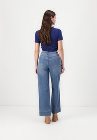 Široke, visoko pasne modre jeans hlače z dvema zadnjima žepoma in zadrgo, v kombinaciji s srajco s kratkimi rokavi v mornarsko modri barvi.