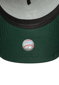 Grüne Baseballmütze mit schwarzem Schirm, auf der Vorderseite mit einem runden MLB-Logo-Aufkleber. Texturiertes Material mit sichtbaren Nähdetails.