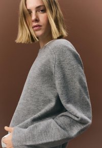 Pulover din lână gri cu decolteu rotund, mâneci lungi și croială lejeră. Textură moale, design minimalist și fără modele vizibile.