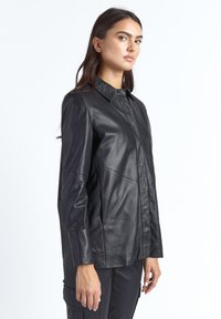 Sort læderjakke med krave, forsynet med knapper foran, lange ærmer og ton-i-ton syninger for et elegant look.