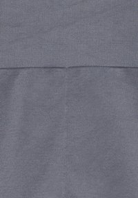 Gros plan sur un tissu gris avec deux motifs tricotés distincts séparés par une couture horizontale et une couture verticale traversant la partie inférieure.
