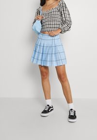 Jupe plissée à carreaux bleus, associée à un crop top à carreaux noir et blanc. Les accessoires comprennent un sac bleu clair et des baskets noires aux semelles blanches.