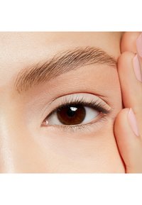 Gros plan sur un œil marron avec de longs cils, un léger maquillage sur les paupières, et des sourcils bien entretenus. Une main touche doucement la joue.
