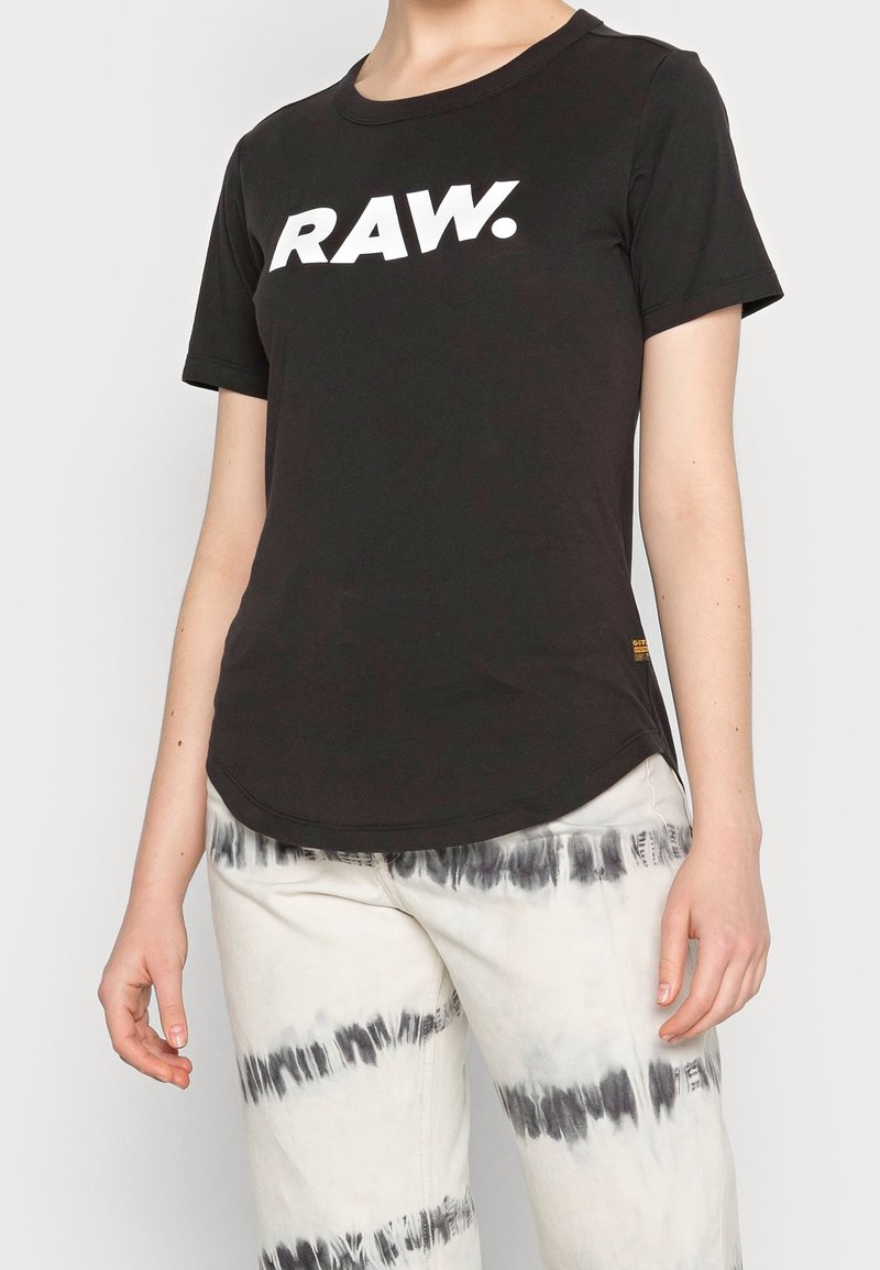 Černé bavlněné tričko s krátkým rukávem, na přední straně s velkým bílým logem "RAW." Zakulacený spodní lem a minimální akcenty.