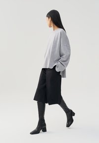 Sudadera gris de gran tamaño, pantalones cortos anchos negros y botas de tacón altas negras. Texturas suaves, ajuste relajado y diseño minimalista.