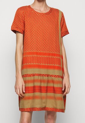 Frau trägt ein kurzärmeliges, knielanges Kleid mit orangefarbenen und beigen geometrischen und gestreiften Mustern.