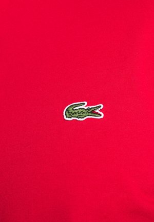 Green embroidered crocodile logo on bright red fabric background, centered and clear.