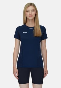 Marinblå sporttröja med korta ärmar, kröka sömmar och reflekterande detaljer. Kombineras med mörka shorts i elastiskt material.
