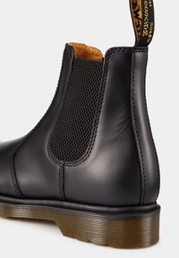 Bottine Chelsea en cuir noir avec panneau latéral élastique, doublure intérieure jaune et semelle translucide rainurée avec languette de tirage marquée à l'arrière.