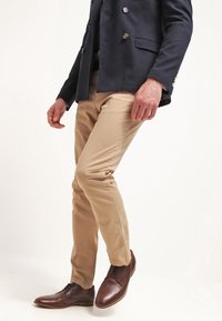 Beige trousers paired with a navy double-breasted jacket. Brown leather shoes with laces. Smooth fabric texture visible.