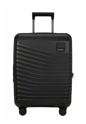 Valise rigide noire avec motifs ondulés horizontaux, quatre roues pivotantes, poignée rétractable et logo Samsonite en haut à droite sur le devant.