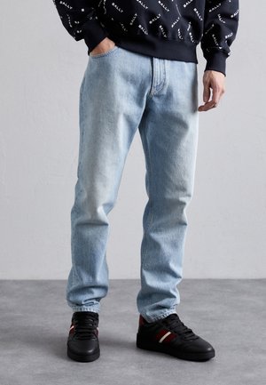 Osoba nosząca jasnoniebieskie dżinsy, czarne trampki z czerwono-białymi paskami oraz czarną bluzę z białym wzorem tekstu.