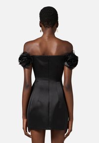 Abito in satin nero con design senza spalline, caratterizzato da dettagli floreali sulle maniche e chiusura con zip sul retro.