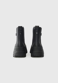 Botas negras de tobillo con parte superior texturizada, suela de goma y tirador trasero. Presenta una marca en el talón y una suela gruesa con un diseño estampado.