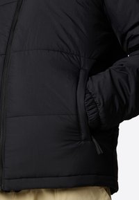 Chaqueta acolchada negra con un acabado texturizado, cierre con cremallera, puños elásticos y bolsillos laterales. Aislada para proporcionar calor, con un forro interior suave.