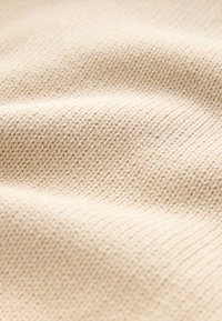 Tissu beige tricoté présentant un motif texturé avec un tissage fin et régulier, affichant des plis et des ondulations doux à la surface.