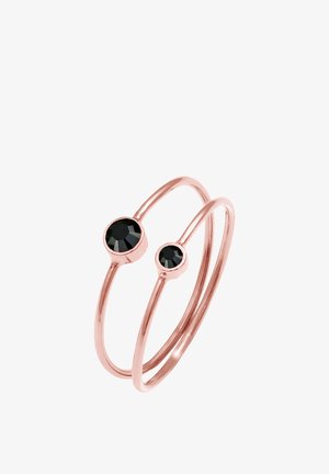Pierścionek z podwójną obrączką w kolorze różowego złota, ozdobiony dwoma okrągłymi czarnymi kryształami, z których jeden jest większy, a drugi mniejszy, o gładkim, błyszczącym wykończeniu.