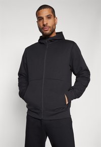 Svart zip-up hoodie i mjukt material, med huva, ribbade ärmslut och sidofickor. Enkelt design utan mönster eller detaljer.