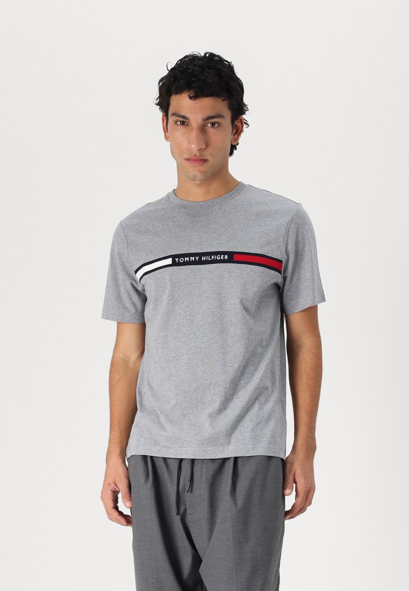 Grå bomulds t-shirt med rund halsudskæring, korte ærmer og et horisontalt stribet logo i hvid, sort og rød på tværs af brystet.