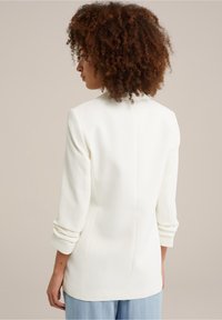 Biała dopasowana marynarka z długimi rękawami, podwiniętymi mankietami i gładką fakturą. Posiada szew z tyłu dla dopasowanego kształtu i subtelnego designu.