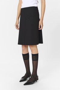 Jupe noiretailleur avec une coupe évasée, associée à des chaussettes noires transparentes mi-hautes avec un motif floral et un bord festonné, et des chaussures noires à talons pointus.