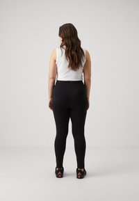 Black leggings and a white sleeveless top, featuring a fitted design. The model has long hair and wears black shoes with red accents.
