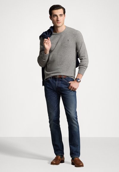 Grå strikket sweater, blå denim jeans, brune lædersko. Casual design med et logo på sweateren og et ur på håndleddet.