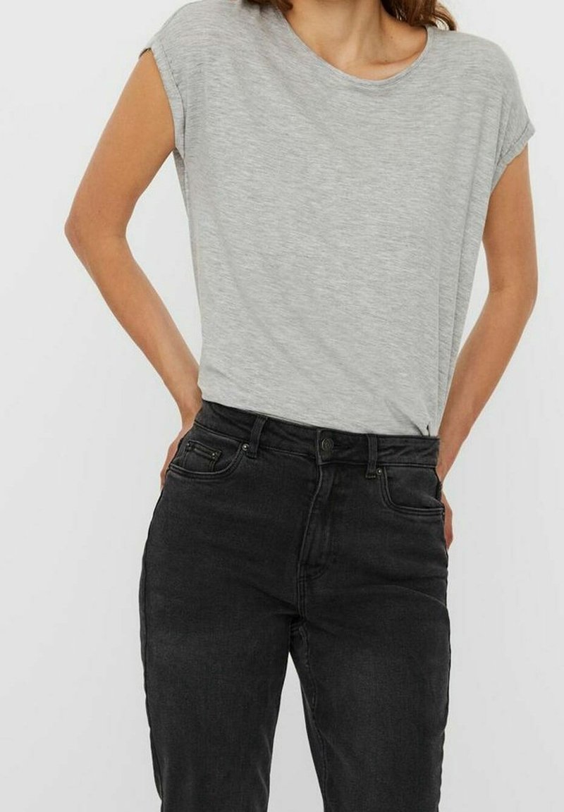 Donna che indossa una maglietta a maniche corte grigia chiara infilata in jeans neri a vita alta con le mani appoggiate sui fianchi.