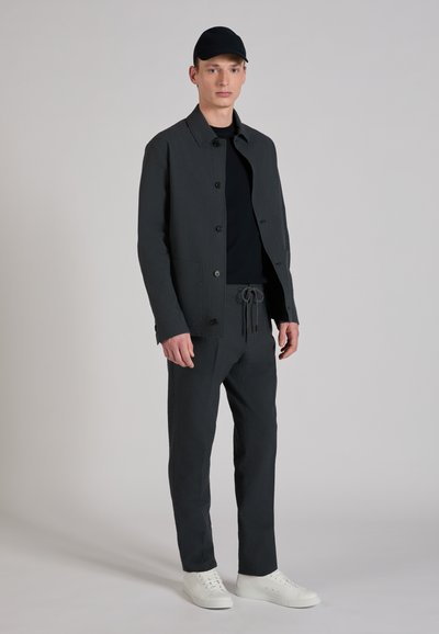 Gray textured jacket with a collar and buttons, paired with matching pants. White sneakers complete the outfit. Black cap worn on the head.