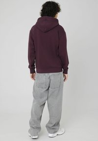Sweat à capuche bordeaux avec grande capuche, poignets et ourlet côtelés. Jean gris ample avec poches arrière, porté avec des baskets blanches. Fond uni.