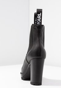 Black heeled ankle boot with smooth leather upper, rounded toe, and textured block heel. Features pull tab with "KARL" branding.